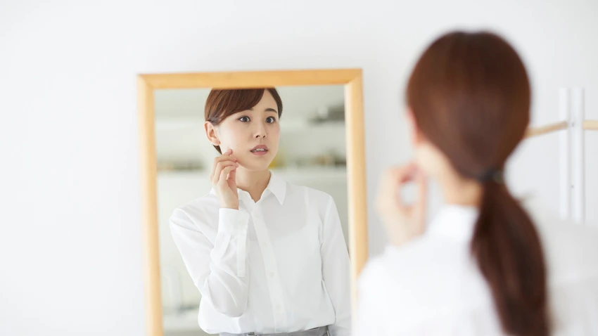 鏡に映る自分の顔を指で触れながら、真剣な表情で確認する女性。